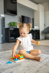 Cute caucasian little girl playing on the floor at home with eco wooden toys. Montessori toy. The...