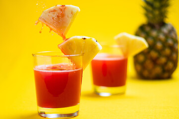 Pineapple juice in glass closeup near sliced fruit with spash and dripping liqid for summer vibes.