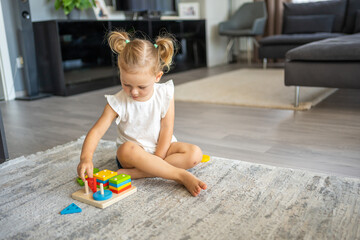 Cute caucasian little girl playing on the floor at home with eco wooden toys. Montessori toy. The child playing educational games.