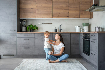 Little girl and happy mother with a cup of milk have a fun at home kitchen 