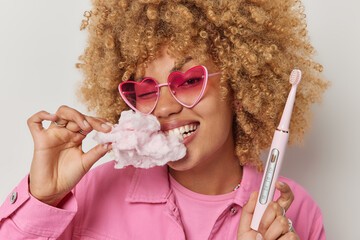 Close up shot of blonde curly haired woman eats sweet food harmful for teeth bites delicious sugary...