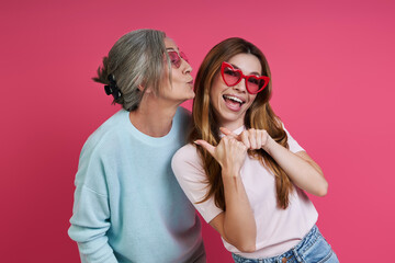 Playful mother and adult daughter in funky eyeglasses having fun against pink background