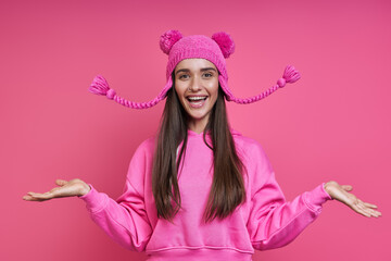 Excited young woman in hooded shirt playing with her funky hat against pink background