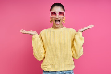 Playful young woman in yellow sweater and funky glasses gesturing against colored background