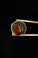 Warm rolls with black rice Sushi with red fish rice, shrimp, lettuce on a black background. Roll in sticks.