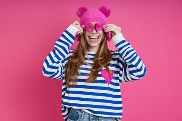 Happy young woman playing with her pink while standing against colored background