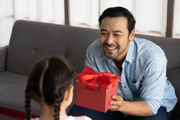 Child Asian girl give a present to his dad while smile, hug and kiss inside of the living room. Happy moment with male parent, family relationship. Father day