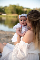 mom with a newborn baby sits on the beach, on the sand. mom holds a newborn baby in her arms.