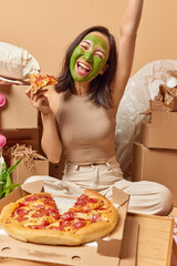 Vertical shot of positive young Asian woman undergoes beauty procedures eats tasty pizza during...