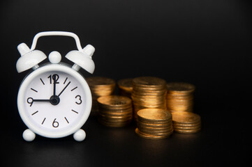 White alarm clock with gold coins isolated on dark background. Copy space and business concept