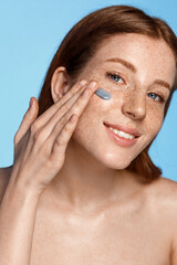 Skin care. Vertical portrait of redhead woman applying clay mask, facial nourishing cream or daily...