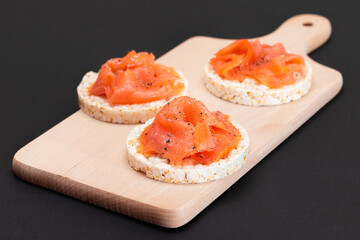 Tasty Rice Cake Sandwiches with Fresh Salmon Slices on Wooden Cutting Board. Easy Breakfast and...