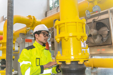 Asian engineer wearing glasses working in the boiler room,maintenance checking technical data of heating system equipment,Thailand people