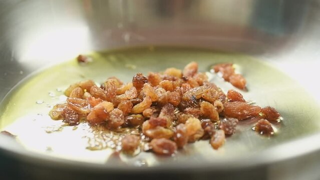 The cook adding raisins into frying pan with olive oil and cumin seeds.
