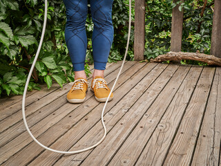 workout with a heavy jump rope - male legs in compression tights on a wooden deck, backyard fitness concept