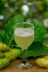 Noni juice in glass and noni fruit with green leaf on rustic wooden and blur background. 