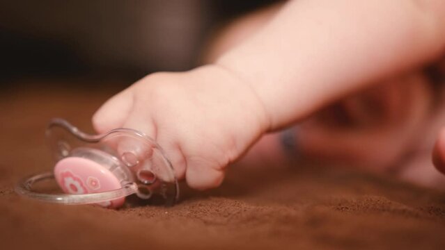 The baby takes a pacifier in his hand