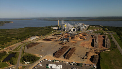 Aerial view showing industrial factory with smoking stacks near natural river during sunny day - Fray Bentos,Uruguay