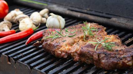 Beef steaks cooking on the charcoal grill with chili pepper, tomatoes, garlic and mushrooms for bbq sauce.