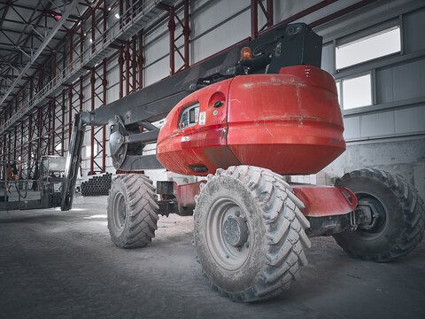 Articulated telescopic elevator. Boom lift picker inside industrial building. Man lifting hydraulic platform parked. Red telehandler at construction site