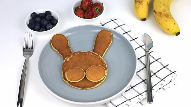 American pancakes decorated with muzzles of animals with strawberries, blueberries and bananas. Food for kids, playful and creative. View from above.