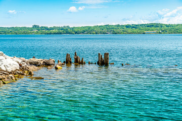 Fototapeta na wymiar Landscape of the Huron Lake water and old withered wooden dock posts or marina wreck at sunny day in Georgian Bay near Spirit Rock Conservation Area at Wiarton, Ontario, Canada.