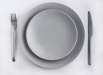 Grey empty plates with silver cutlery on the white table decorated by dried flowers