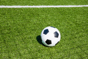 Fototapeta na wymiar Football soccer sport background. Green artificial turf soccer field with white line, shadow from football goal net and soccer ball on sunny day outdoors. Top view