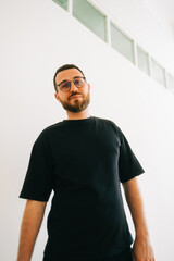 Obraz premium Portrait of stylish caucasian man in eyeglasses and black t shirt in bright living room.