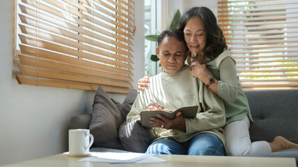 Happy elderly couple relaxing together on comfortable couch at home. Elderly love, family, retirement lifestyle concept.