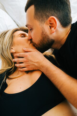 Happy young couple lying on a bed, husband kissing wife and hug. 