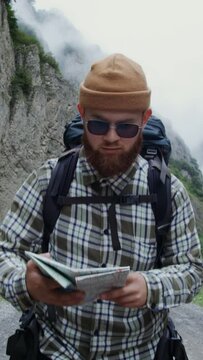 Caucasus. A young man studies map while standing on wide road among the rocks