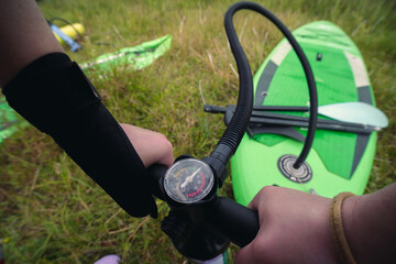 Girl hand close up inflating stand up paddle sup board with manual pump at green grass background....