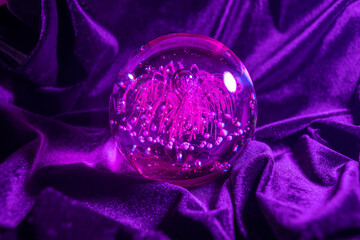 Closeup shot of a purple magic glass ball on the purple velvet cloth,divination concept