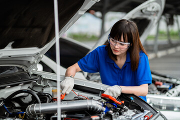 Asian woman mechanic checking the engine of a car at a garage. Auto repair, car service and maintenance concepts. Car inspection. Auto repair shop. Service concept. Auto repair service concept.