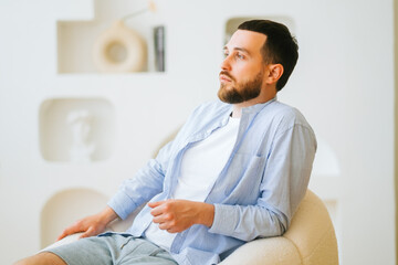 Portrait of attractive caucasian guy wearing stylish casual clotting sitting in armchair.
