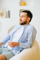 Portrait of attractive caucasian guy wearing stylish casual clotting sitting in armchair.