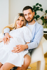Portrait of future mother and father. Husband hugs pregnant wife. Happy family resting at home