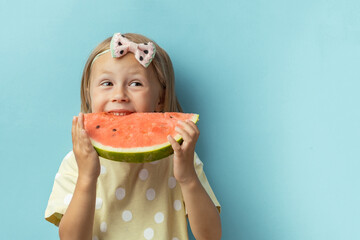 Cute little girl enjoying big slice of juicy red watermelon on the blue background. Portrait of...
