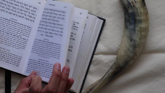 07-07-2022. jerusalem-israel. A boy's hand flips through a Rosh Hashanah prayer book, against the backdrop of a tallit and shofar