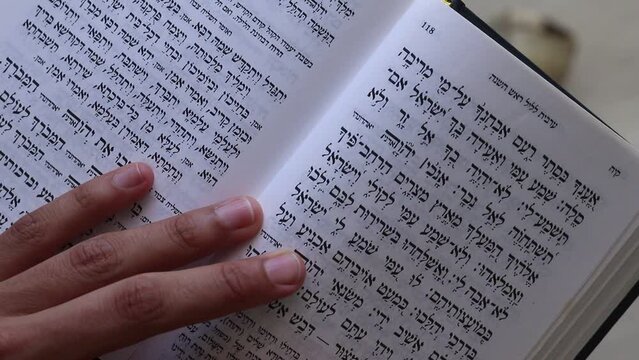 07-07-2022. jerusalem-israel. A boy's hand flips through a Rosh Hashanah prayer book, against the backdrop of a tallit and shofar