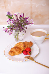 
Coffee cup and sweet croissant with fresh strawberry on white table, decorated with beautiful flower bouquet
