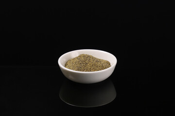 Ground black pepper in a white plate on a dark table with reflection. Close-up