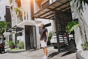 Young businessman walking out of his modern home with garage and car