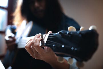 Close up on hand of asian musician who have long hair is playing acoustic guitar and change chord with his fingers solo the music in dark room with lighting.