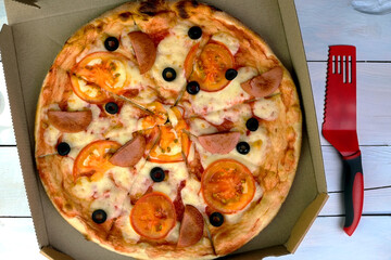Fresh round pizza with tomatoes, sausage, mozzarella and olives in cardboard box. - 520395647