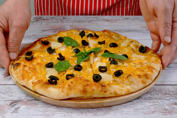 Chef puts on table homemade pizza with cheese, chicken meat, olives and basil leaves. Tasty unhealthy fast food snack of Mediterranean food. - 520395665
