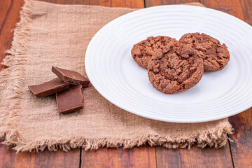 Fototapeta na wymiar Cookies de chocolate com leite em fundo rústico. pedaços de chocolates e cokkies em um prato branco
