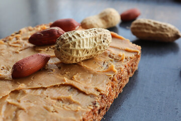 Peanut butter on bread with peanuts or groundnuts in the background 