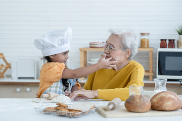 Happy family Asian grandmother and little grandchild spend time together at kitchen, knead dough...